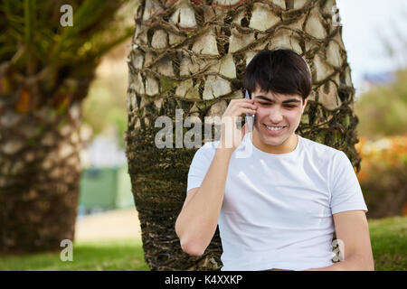 Front portrait of young happy man sitting under tree talking on mobile Stock Photo