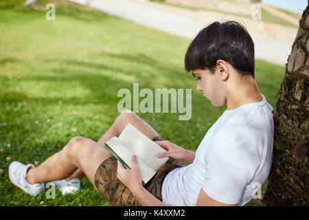 Portrait of young man sitting on grass reading book Stock Photo
