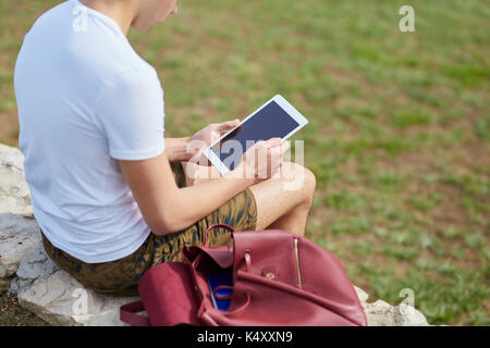 Back portrait of man sitting on wall using tablet Stock Photo