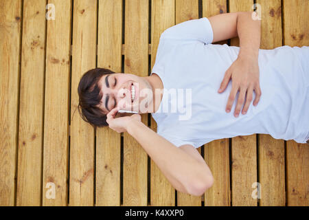 Aerial portrait of young happy man lying on wooden planks talking on mobile Stock Photo