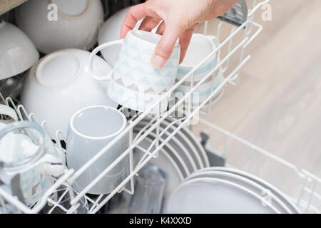 Close Up Of Woman Loading Crockery Into Dishwasher Stock Photo