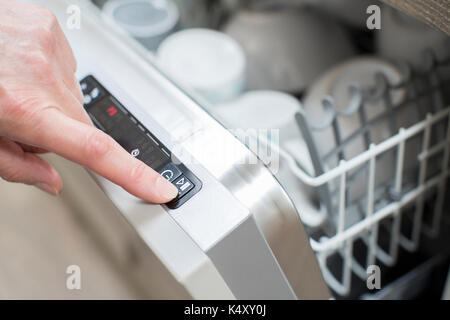 Close Up Of Woman’s Hand Pressing Start Button On Dishwasher Stock Photo