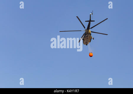 Firefighter helicopter in flight carrying an water bucket Stock Photo