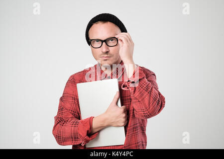 A young programmer in a black hat is holding a laptop in his han Stock Photo