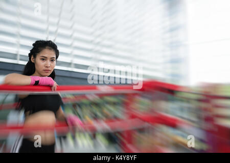 young woman prepare for exercise in fitness center. female boxer posing in boxing ring in gym. sporty asian girl resting after working out in health c Stock Photo