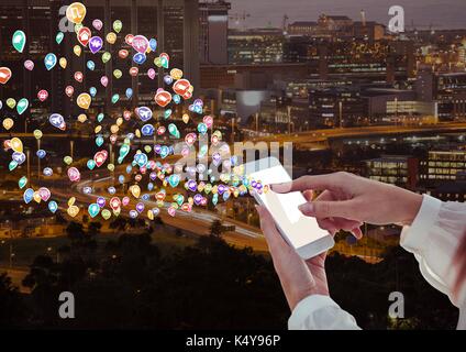 Digital composite of woman hands with phone with application icons coming up form it. Blurred city at night Stock Photo