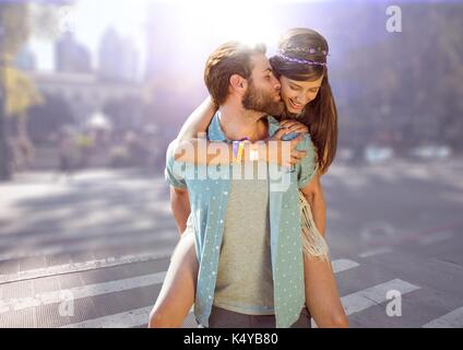 Digital composite of Couple piggy back against blurry street with flare Stock Photo