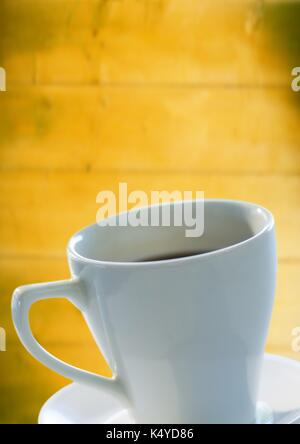 Digital composite of White coffee cup and saucer against blurry yellow wood panel Stock Photo
