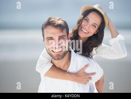 Digital composite of Couple piggy back against blurry beach Stock Photo