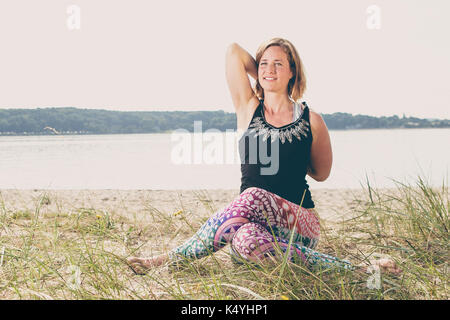 Young fit woman exercises yoga on the beach dune early morning in Germany Stock Photo