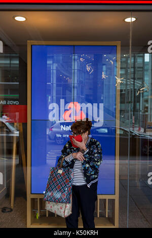 A woman uses her smartphone for a private conversation outside the branch of Natwest Bank on Victoria Street, on 6th September 2017, in London, England. Stock Photo