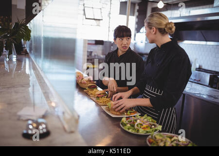 young female chefs talking while preparing food at kitchen counter in coffee shop Stock Photo