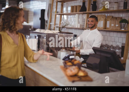 Smiling waiter looking at female customer standing at counter in coffee shop Stock Photo