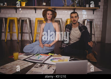 Portrait of young creative professionals sitting on floor with papers at coffee shop Stock Photo