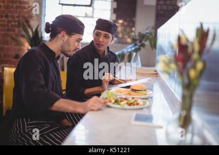 Young wait staff discussing over clipboard and food while sitting at counter in coffee shop Stock Photo
