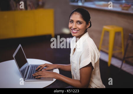 Side view portrait of smiling young woman using laptop at table in coffee shop Stock Photo