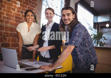 Portrait of smiling young creative team standing with laptop in coffee shop Stock Photo