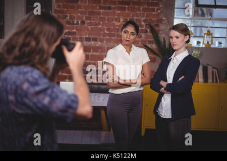 Male photographer clicking picture of confident female colleagues standing with arms crossed at coffee shop Stock Photo