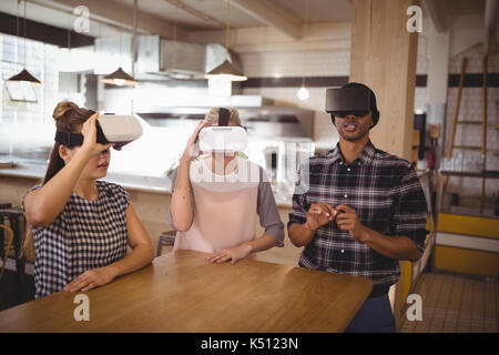 Young friends sitting with virtual reality headsets at table in coffee shop Stock Photo