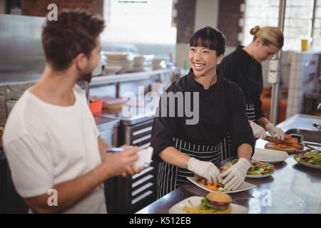 Cheerful waiter and female chef working in kitchen at cafe Stock Photo