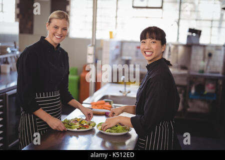 Portrait of smiling female chefs with fresh food in plates on kitchen counter at cafe Stock Photo