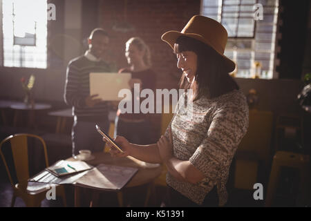 Smiling woman using smartphone against colleauges standing at coffee shop Stock Photo