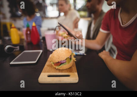 Midsection of young woman using smartphone while sitting with burger at table in coffee shop Stock Photo