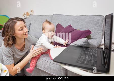 Nine months old baby girl playing with her mother and trying to touch the laptop Stock Photo