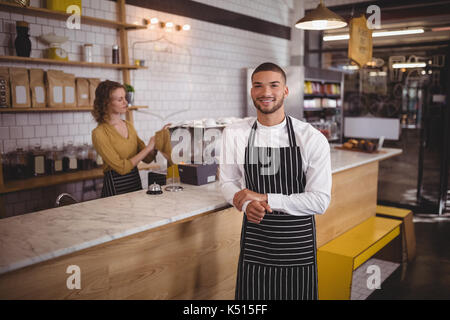 Portrait of waiter standing by counter while waitress working at coffee shop Stock Photo