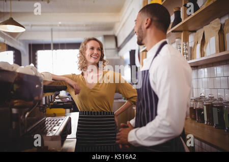 Smiling young waiter and waitress standing by espresso maker in coffee shop Stock Photo