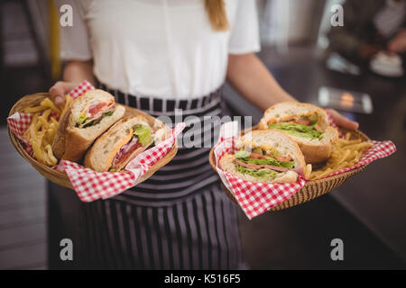 Midsection of waitress holding fresh fast food in wicker baskets at cafe Stock Photo