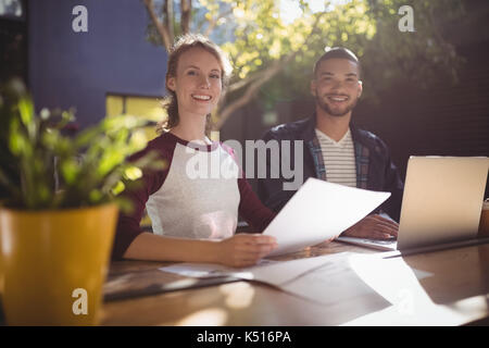 Portrait of smiling young creative professionals sitting with laptop at table in coffee shop Stock Photo