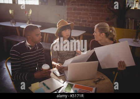 High angle view of young creative team sitting with laptop and papers at coffee shop Stock Photo