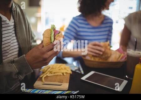 Midsection man holding fresh hamburger while sitting at table in cafe Stock Photo