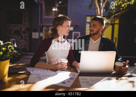 Young creative professionals talking while sitting with laptop at table in coffee shop Stock Photo