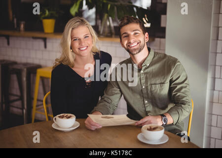 Portrait of smiling young couple sitting with coffee cups and menu at table in cafe Stock Photo