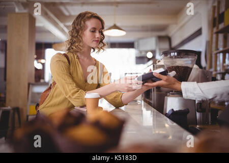 Young female customer paying through card at counter in coffee shop Stock Photo