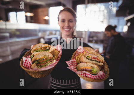 Portrait of smiling young waitress serving fresh burgers in baskets standing at coffee shop Stock Photo