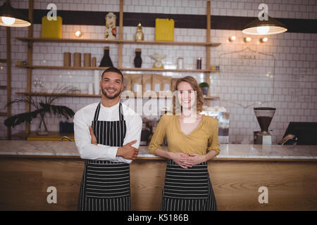 Portrait of smiling young wait staff standing against counter at coffee shop Stock Photo