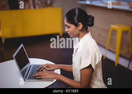 Side view of young woman typing on laptop while sitting at table in coffee shop Stock Photo