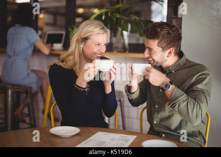 Cheerful young couple drinking coffee while sitting at table in cafe Stock Photo