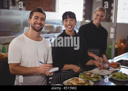 Portrait of waiter with female chefs standing with food in kitchen at cafe Stock Photo