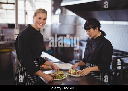 Portrait of smiling female chefs preparing fresh Greek salad at kitchen counter in cafe Stock Photo