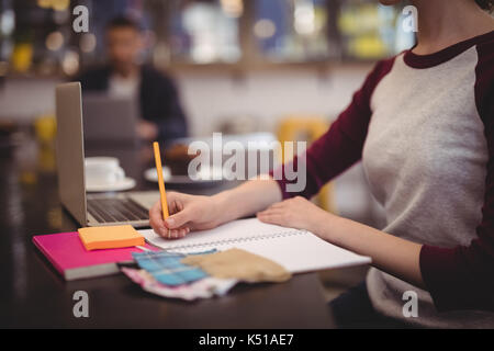 Midsection of design professional writing in dairy while sitting at table in coffee shop Stock Photo