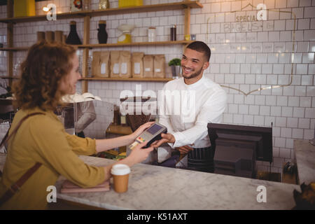 Smiling young woman paying through card to waiter at counter in coffee shop Stock Photo