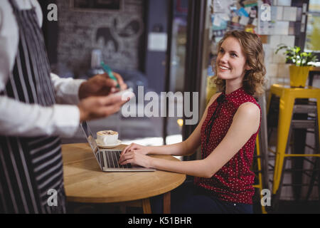 Midsection of waiter holding notepad while standing by smiling young female customer at coffee shop Stock Photo