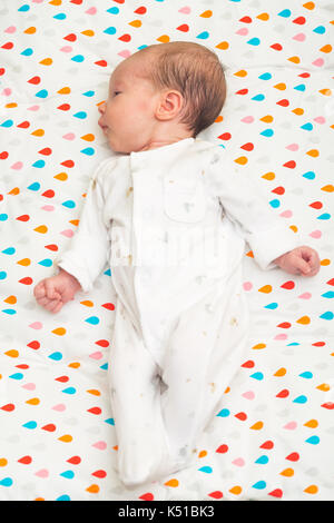 Newborn baby dressed in white sleeping on her back, head to the side Stock Photo