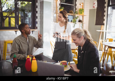 Young man ordering food to waitress while sitting with female friend at cafe Stock Photo