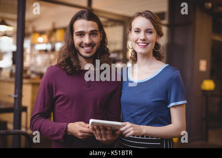 Portrait of confident young waitress and man holding digital tablet at coffee shop Stock Photo