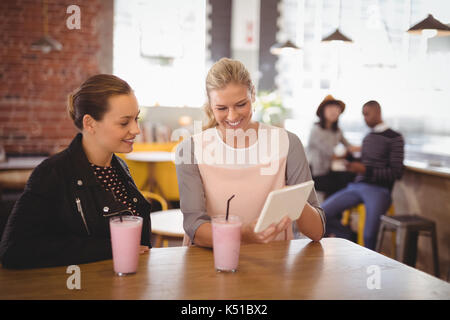 Smiling young female friends using tablet computer while sitting at table in coffee shop Stock Photo